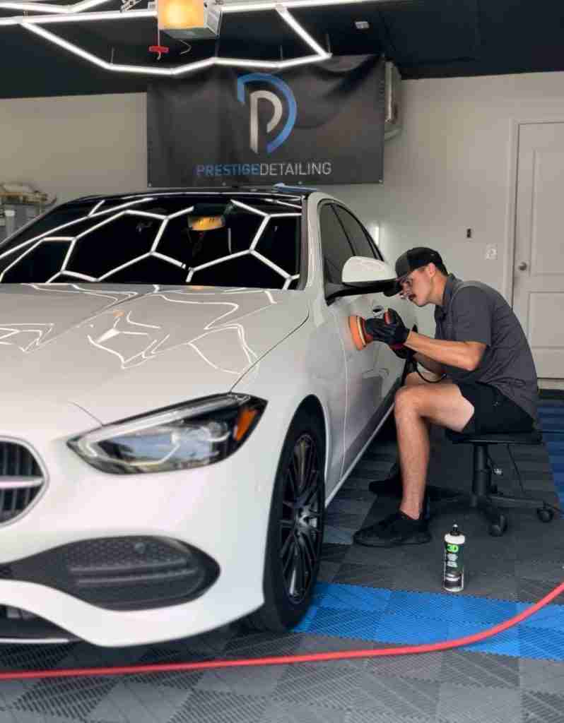 Technician performs paint correction on a white car in Prestige Detailing’s Cape Coral shop bay